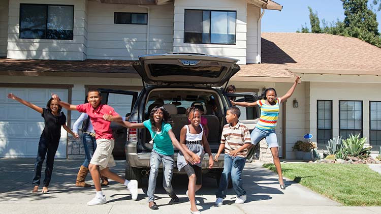 A gathering of young children frolic behind an open SUV parked in the driveway.